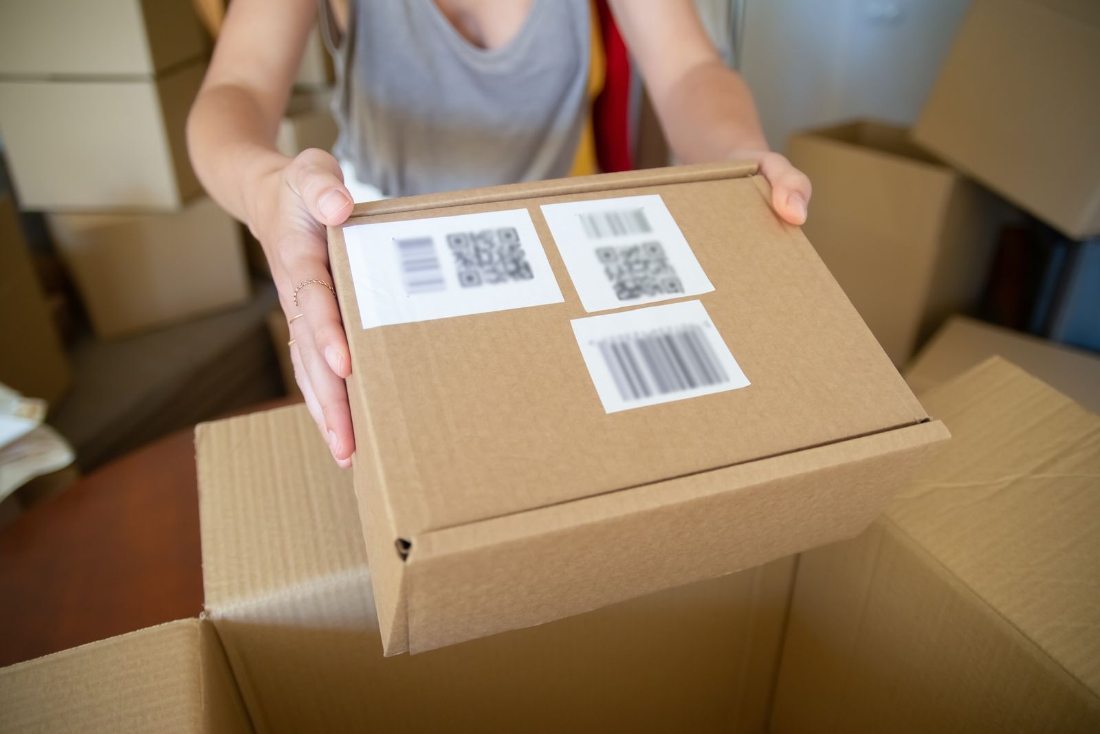 Caja de cartón con etiquetas de código de barras y QR pegadas, sostenida con las manos antes de despacharla