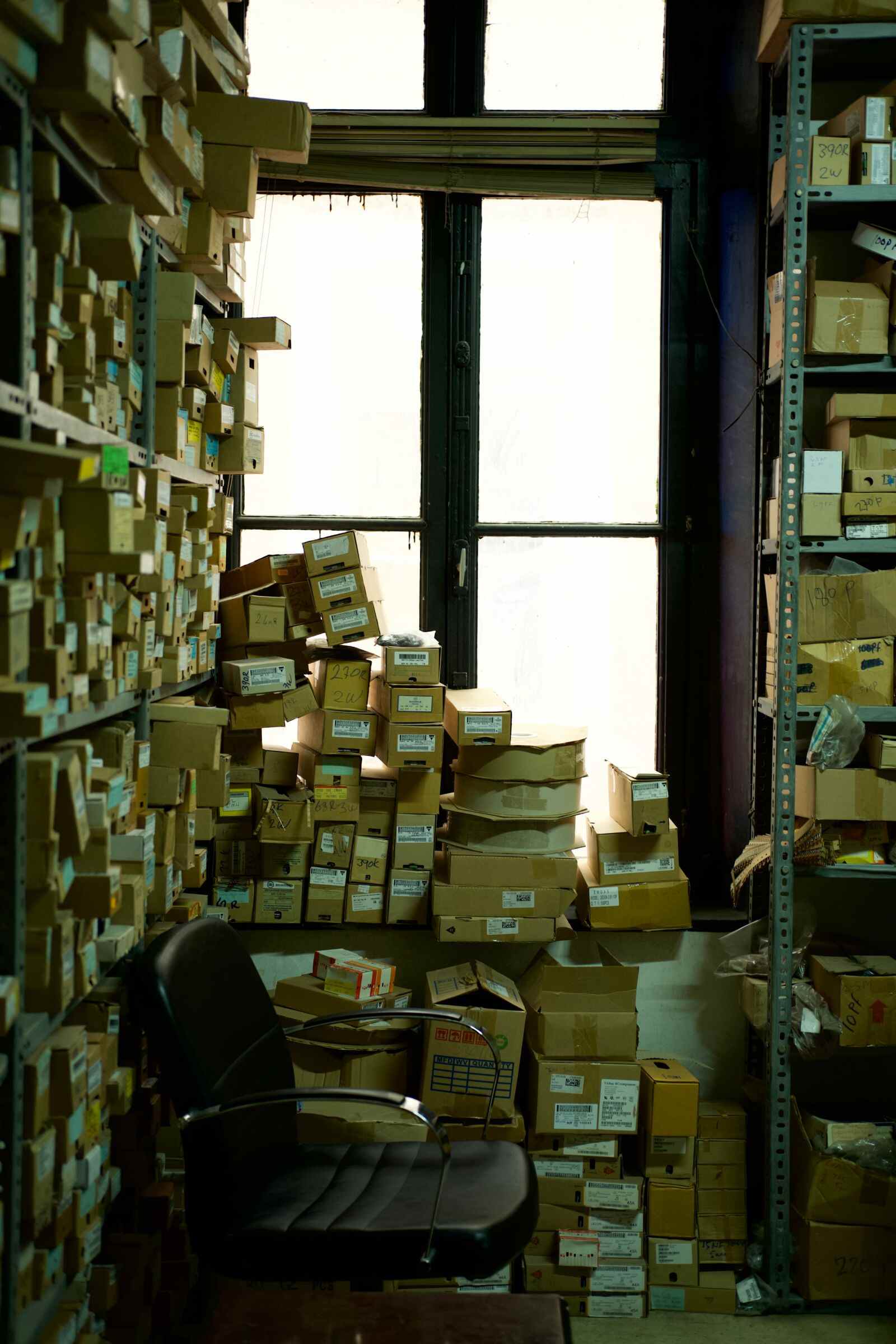 Depósito chico repleto de cajas y productos apilados en estanterías, con luz natural entrando por la ventana