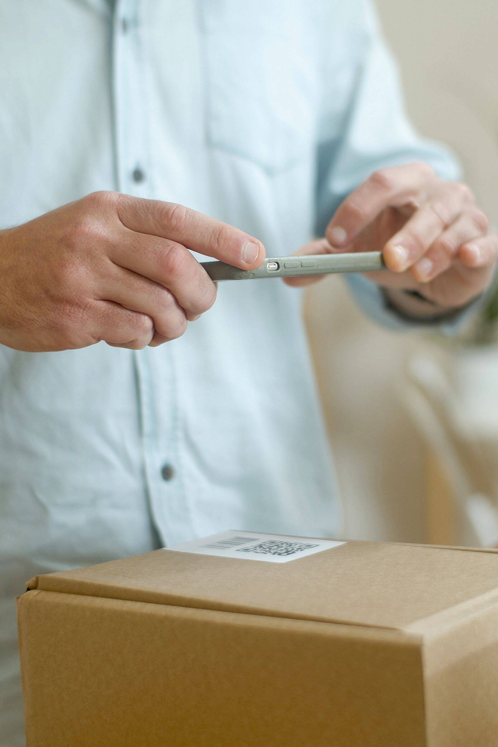 Mano escaneando el código QR de una caja con la cámara de un celular, sobre una mesa de trabajo